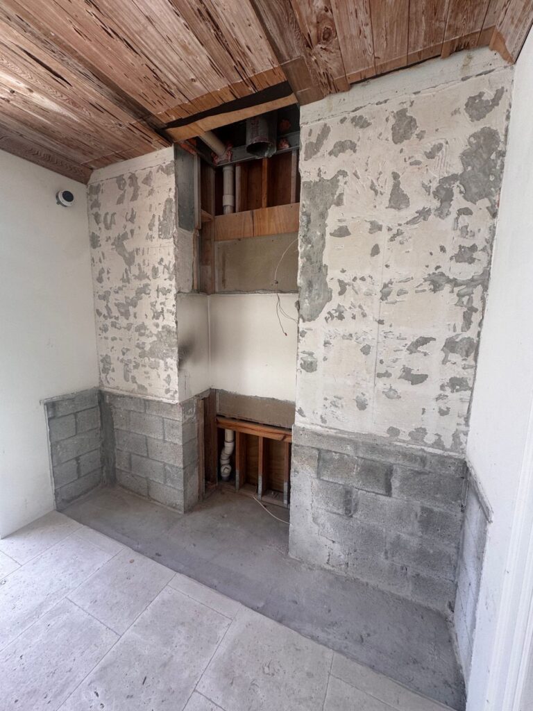 Wall and soffit opened up in a selective demolition, exposing framing and block while the surrounding finishes stay intact.