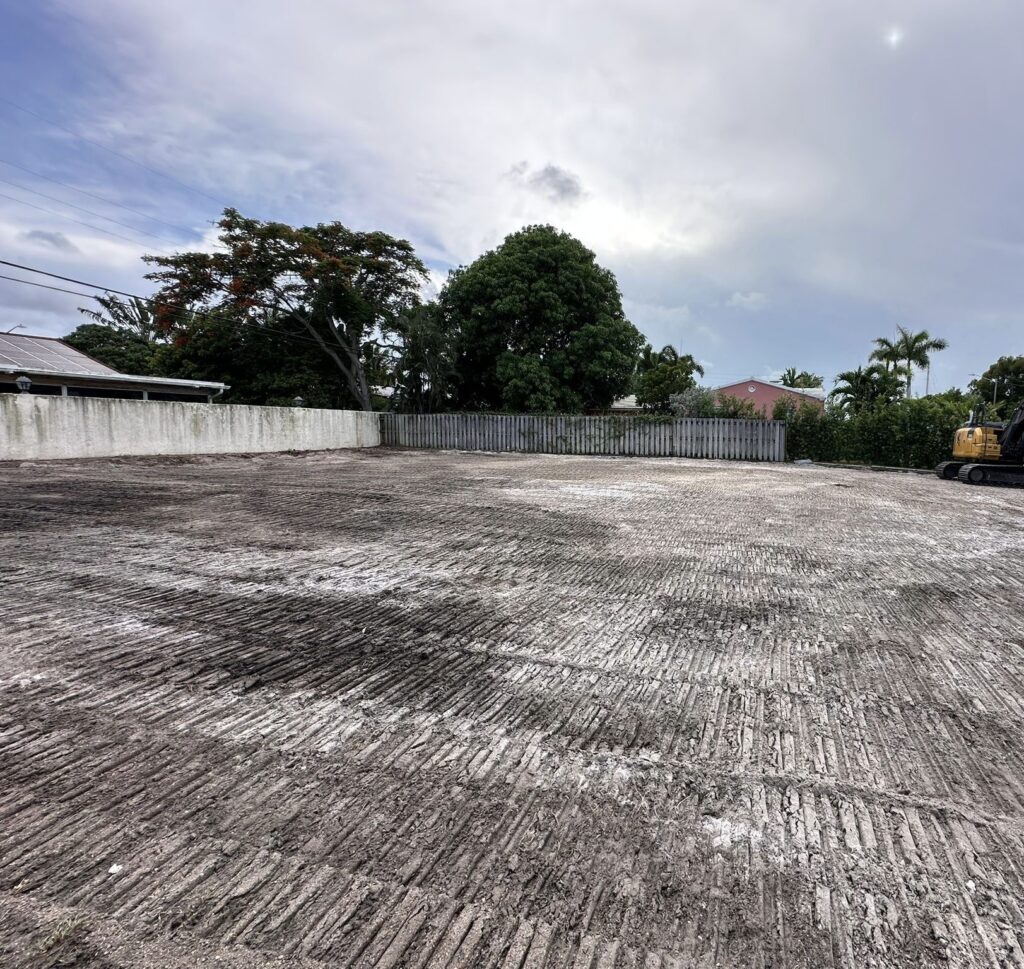 Residential lot cleared to bare ground and tracked flat, with the existing perimeter walls and neighboring property left untouched.