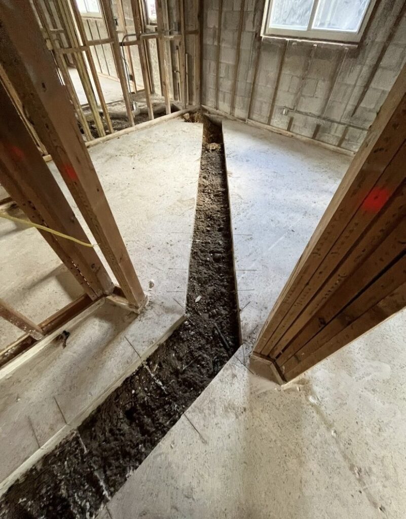 Utility trench cut and excavated through an interior slab while the surrounding framing and block walls stay fully intact.